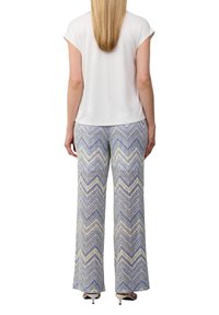 Haut blanc à manches courtes associé à un pantalon large avec un motif en zigzag dans des nuances de violet, bleu et crème.