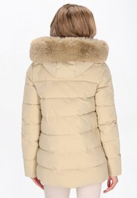 Jachetă puffer bej cu glugă din blană artificială, design căptușit, mâneci lungi și tiv curbat. Material neted, ușor, cu un luciu subtil.