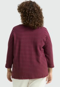 Haut à manches longues rayé maroon et rose avec un col rond. Il présente une coupe décontractée et un tissu doux en texture. Couture visible le long de l'ourlet.
