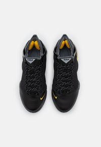 Scarpe da ginnastica nere con accenti gialli, caratterizzate da una punta in pelle texturizzata, parte superiore in mesh e fodera grigia a contrasto. Lacci con dettagli riflettenti.