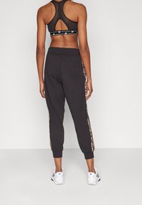 Černá sportovní podprsenka s kříženými ramínky na zádech, doplněná černými tepláky s leopardím potiskem na bočních pruzích a bílými sportovními botami.