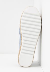 Ljusblå espadrill med en vit gummisula, försedd med en jute-rep detaljer runt kanten och en texturerad, räfflad yta på sulan.