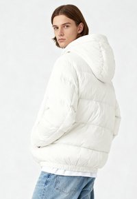 Giacca a vento bianca con cappuccio, design trapuntato e polsini elastici. Indossata sopra una camicia bianca, abbinata a jeans in denim azzurro chiaro.