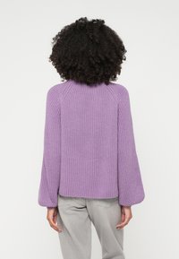 Lila rebrast pulover z visokim ovratnikom, napihnjenimi rokavi in sproščenim krojem. Nosi se z svetlo sivo visokim pasom.