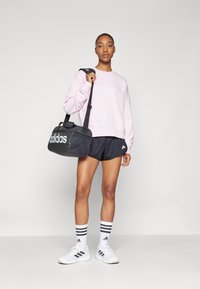 Černá sportovní taška s bílým logem "adidas", růžová mikina, černé šortky, bílé boty a pruhované ponožky. Neformální sportovní oblečení a doplňky.