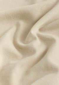 Beige kangas, jolla on sileä, hieman venyvä rakenne ja hienovarainen neulekuvio. Rypistetty osoittamaan laskostusta ja pehmeyttä.