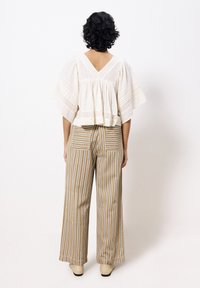 Kurzarmpullover aus weißer Baumwolle mit V-Ausschnitt und gerafftem Design, kombiniert mit weit geschnittenen, beigefarbenen und weißen gestreiften Hosen.