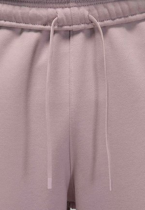 Primo piano della vita di pantaloni della tuta malva con coulisse abbinate che pendono liberamente sulla texture del tessuto.