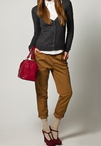 Grauer Cardigan über einem weißen Kragenhemd, braune tapered Pants, cremfarbene Socken und rote High-Heels. Rote Handtasche mit strukturiertem Finish.
