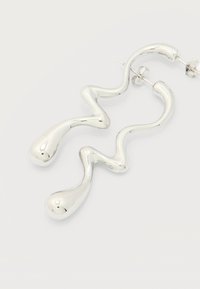 Ζευγάρι λαμπερά ασημένια σκουλαρίκια καρφίτσες με κυματιστό, αφηρημένο σχήμα και στρογγυλεμένες άκρες σε απλό λευκό φόντο.