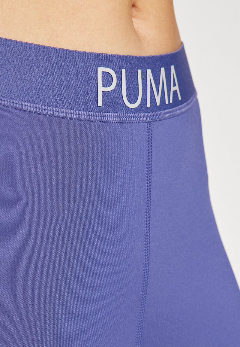 Leggings viola con una texture liscia, una vita alta con "PUMA" in bianco in rilievo e cuciture rinforzate lungo le cuciture.