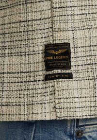 Tissu à carreaux crème et noir avec une finition texturée ; présente une étiquette noire avec "PME Legend" et "Type No : C-46" en lettres dorées.