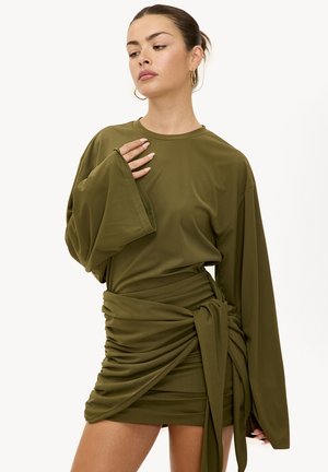 Olijfgroene jurk met lange, wijde mouwen en een getailleerd, geplooid ontwerp. Voorzien van een detail met zijstrik, gemaakt van een gladde, rekbare stof.