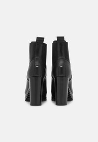 Czarne botki za kostkę z wysokim słupkowym obcasem, wykonane z gładkiej skóry, z elastycznymi bocznymi panelami; detal z logo z tyłu, blisko obcasa.