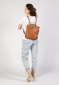 Brauner Leder-Rucksack mit einem strukturierten Design, verstellbaren Trägern, einem oberen Griff und einer glatten Textur. Trägt man auf dem Rücken mit einem lässigen Outfit.