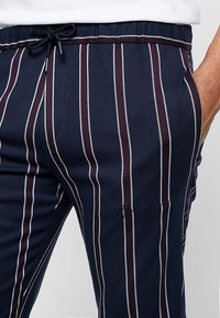 Námořnické pruhované kalhoty s elastickým pasem na šňůrku, které mají střídající se tenké bílé a burgundské pruhy a jemný vyšívaný detail.