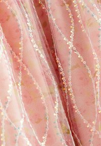 Tela de tul rosa con patrones ondulados de lentejuelas y un delicado ribete de encaje, creando una apariencia estratificada y texturada.