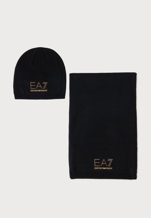 Sort strikket hue og matchende tørklædesæt med gyldne EA7 Emporio Armani logoer på hvid baggrund.
