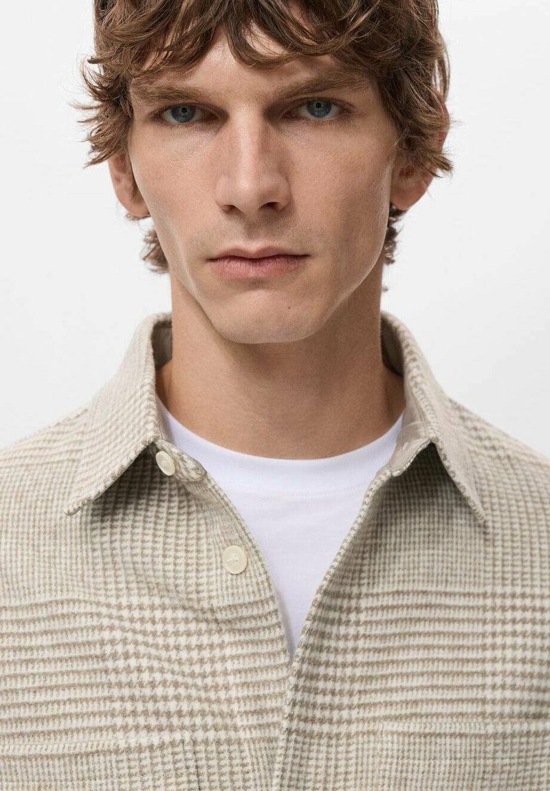 Hellbeiges kariertes Hemd mit Knopfkragen, strukturierter Stoff und einem darunter sichtbaren weißen Unterhemd.