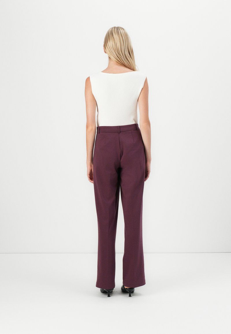 Weißes, geripptes, ärmelloses Top, kombiniert mit burgunderfarbenen, hoch taillierten, ausgestellten Hosen. Schwarze, hohe Schuhe; glatte Textur mit klaren Linien.