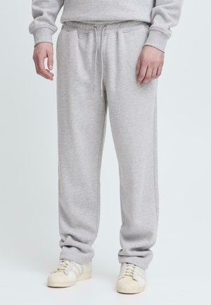 Pantalones de chándal grises hechos de una tela suave, con una cinturilla elástica y cordón ajustable. Se recogen en los tobillos, proporcionando un ajuste relajado.