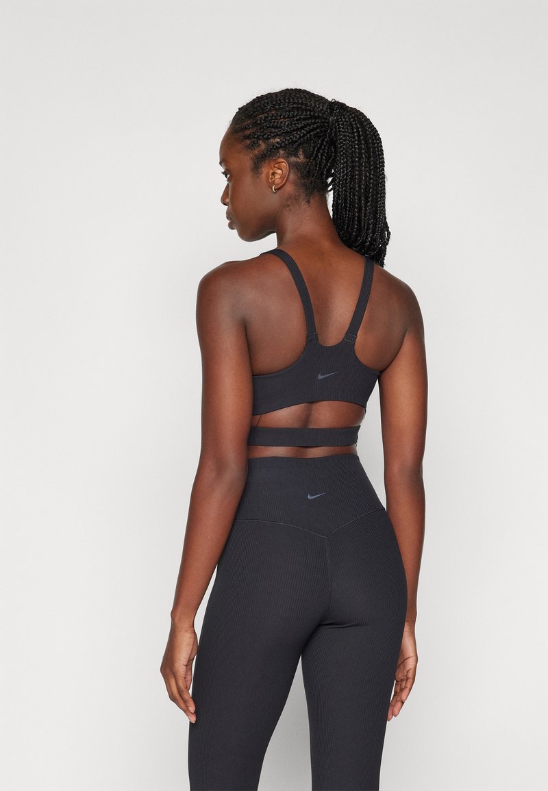 Sujeción deportiva negra con diseño de espalda nadadora y detalle recortado, combinada con leggings negros de cintura alta y canalé, que presentan sutiles acentos de logo.