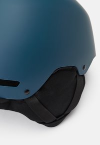 Blauwe helm met een matte afwerking, zwarte stoffen padding, ventilatiesleuven en verstelbare riemen voor een veilige pasvorm.