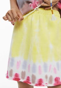 Gonna tie-dye nei colori giallo, bianco e pastello. Vita elastica con nappina decorativa. Tessuto morbido con vestibilità comoda e orlo sfrangiato.