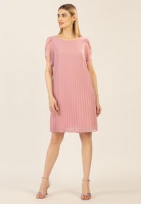 Faltenrockiges pinkes Kleid mit kurzen Puffärmeln und Rundhalsausschnitt, das durch ein fließendes Design und einen leichten Stoff besticht, kombiniert mit Riemchenschuhen.