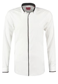Chemise blanche à manches longues boutonnée avec un biais noir le long du col, de la ligne de boutons et des poignets, affichée sur un fond uni.