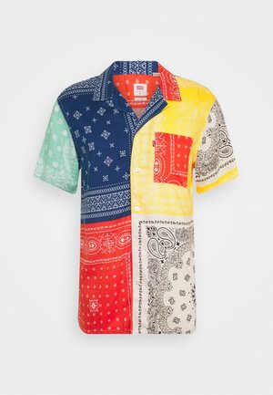 Chemise à manches courtes à boutons avec des patchs imprimés de bandanas multicolores en bleu, rouge, jaune, vert et blanc, avec une poche poitrine rouge.