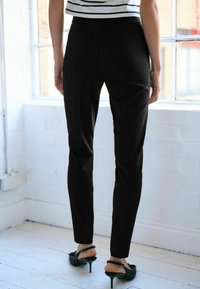 Zwarte op maat gemaakte broeken met een slim fit, met een gladde textuur, details aan de zijnaad en gedragen met zwarte hakken.