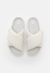 Paire de sandales blanches à glissière avec des larges brides croisées rembourrées et des semelles intérieures perforées et coussinées sur un fond uni.