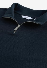 Marineblaues Reißverschlusshemd aus strukturiertem Stoff, mit geripptem Kragen und silbernem Reißverschluss. Das Etikett trägt die Aufschrift "NEXT RELAXED FIT."
