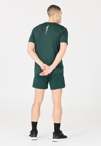 Dunkelgrünes sportliches T-Shirt mit kurzen Ärmeln und passender Shorts, aus leichtem Stoff, mit einem Rückennähtendetail. Schwarze Sportschuhe.