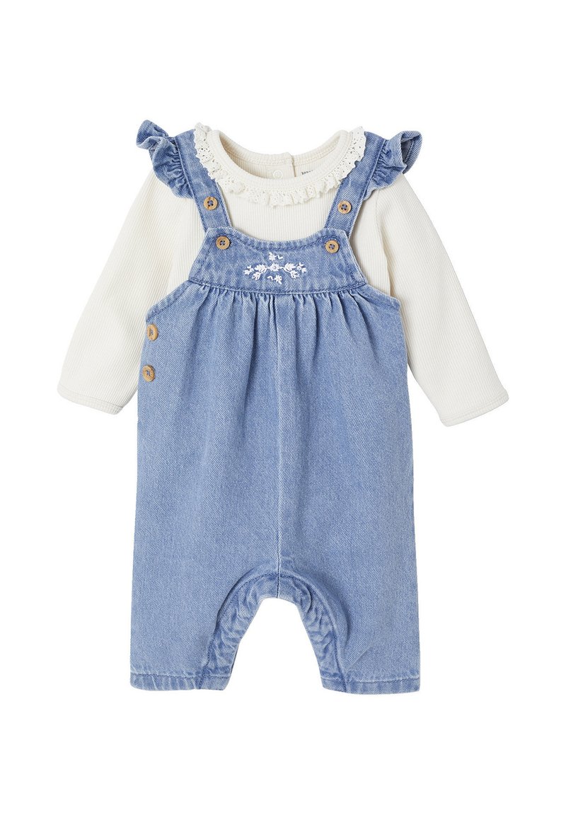 Blaue Denim-Latzhose mit Holzknöpfen, besticktem Blumenmuster auf dem Latz und einem weißen Langarmoberteil mit Rüschenausschnitt.