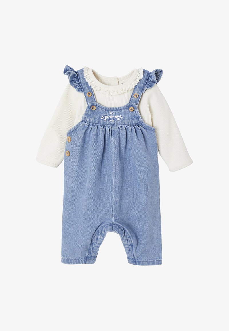 Blaue Denim-Latzhose mit Holzknöpfen, besticktem Blumenmuster auf dem Latz und einem weißen Langarmoberteil mit Rüschenausschnitt.