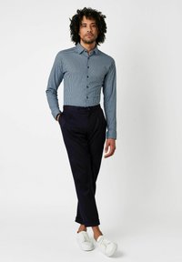 Blau-weißer karierter Langarmhemd, kombiniert mit dunkelblauen Hosen und weißen Sneakers. Besitzt Knöpfe vorne und hochgekrempelte Ärmel.