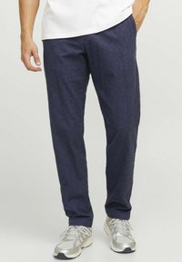 Pantaloni blu navy, dal taglio rilassato, con un motivo testurizzato, abbinati a scarpe da ginnastica grigio chiaro. Il materiale sembra morbido e traspirante.