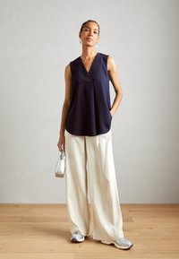 Haut sans manches bleu marine avec un décolleté en V, coupe ample ; associé à un pantalon large crème et des baskets argentées ; portant un petit sac argent.