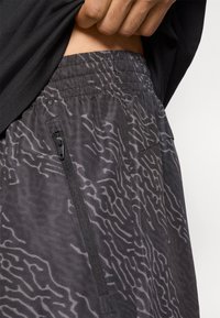 Μαύρο σορτς με σχέδιο και υφή στην επιφάνεια, διαθέτει ελαστική μέση και πλαϊνή τσέπη με φερμουάρ.