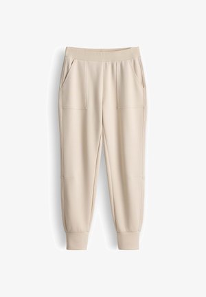 Beige Jogginghosen aus weichem Stoff, mit einem gerippten Bund und zwei Seitentaschen, sowie mit zulaufenden Bündchen an den Knöcheln.