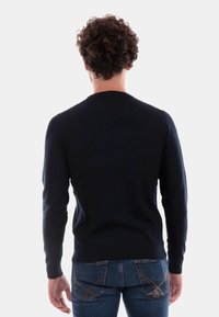 Maglione lavorato a maglia blu navy con maniche lunghe, scollatura a girocollo e polsini a costine. Indossato sopra jeans di jeans chiaro con tasche posteriori angolate.
