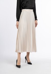 Fustă midi pliată din satin bej soft, cu talie elastică, asociată cu tocuri negre. Materialul texturat creează o siluetă fluidă.
