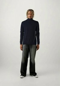 Camisa de gola alta azul-marinho com mangas longas, combinada com jeans largos cinza e ténis pretos com solas brancas. Textura suave, estilo casual.