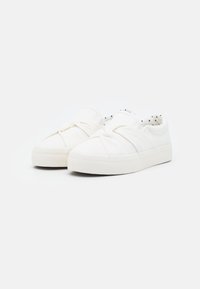 Weiße Slipper mit dicken Sohlen und gerafftem Stoffdetail über der Oberseite, gefüttert mit weißem Stoff, der schwarze Punkte hat.