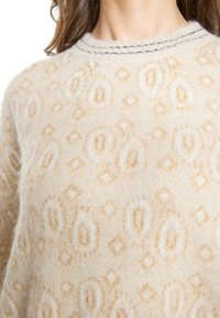 Maglione beige realizzato in morbido tessuto a maglia, con un motivo in rilievo di ovali e diamanti, e cuciture scure attorno al collo rotondo.