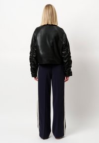 Zwarte leren cropped jas met opgeblazen mouwen, gecombineerd met marineblauwe wijde broek met crèmekleurige zijstrepen. Glad textuur en moderne uitstraling.