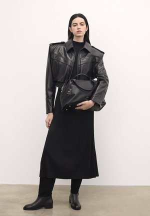 Black leather cropped jacket with shoulder pads, paired with a ribbed black midi dress. The model holds a black leather handbag with gold accents.