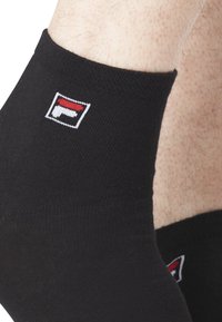 Chaussettes noires à la cheville en tissu lisse avec un petit logo brodé rouge et blanc sur le revers. Présentent un design ajusté autour de la cheville.